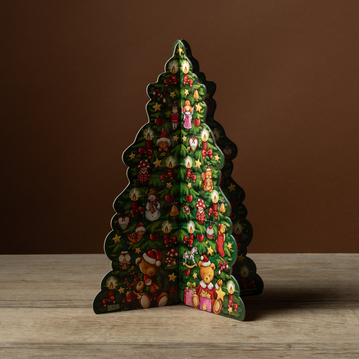 Korsch Verlag Advent Stand-Up Tree with illustrated candles, teddy bears, and 24 numbered doors, displayed on a wooden table.